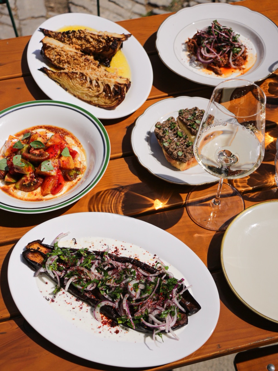 Gedeckter Tisch mit Vorspeisen, Aubergine und Wein im Sonnenlicht